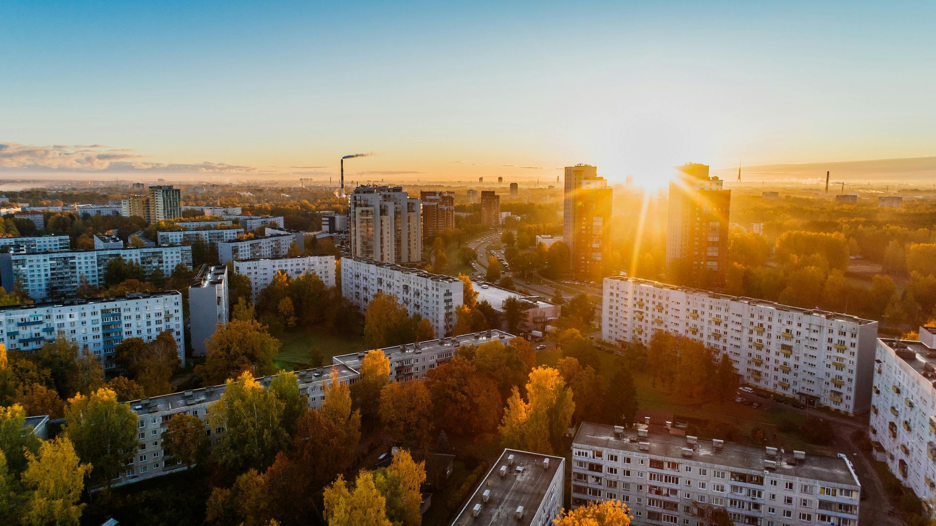 City skyline at sunrise with apartment buildings, trees, and golden sunlight.
