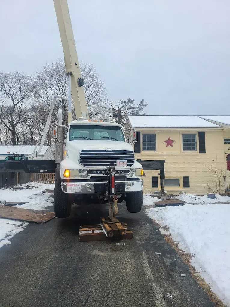 Tow truck lifting a beige utility pole on a snowy residential street near a house with a star on it