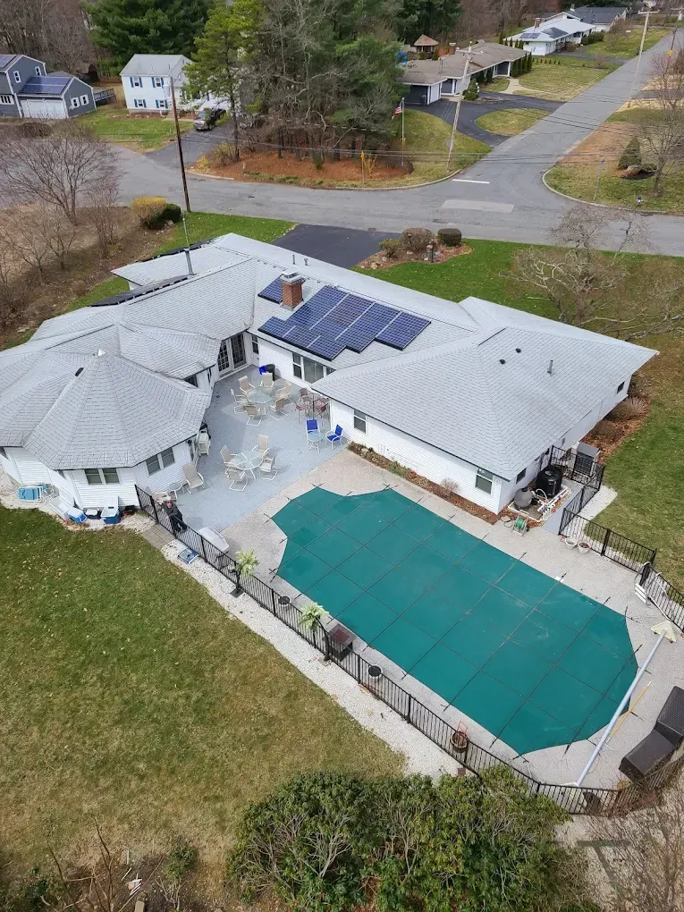 Aerial view of a house with a white roof, solar panels, and a covered backyard pool in a suburban neighborhood.