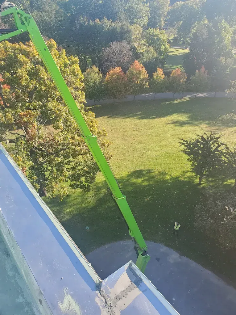 Green crane arm beside a blue building, overlooking a sunny grassy yard and trees