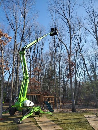 Bright green boom lift extended in a wooded yard under a clear sky