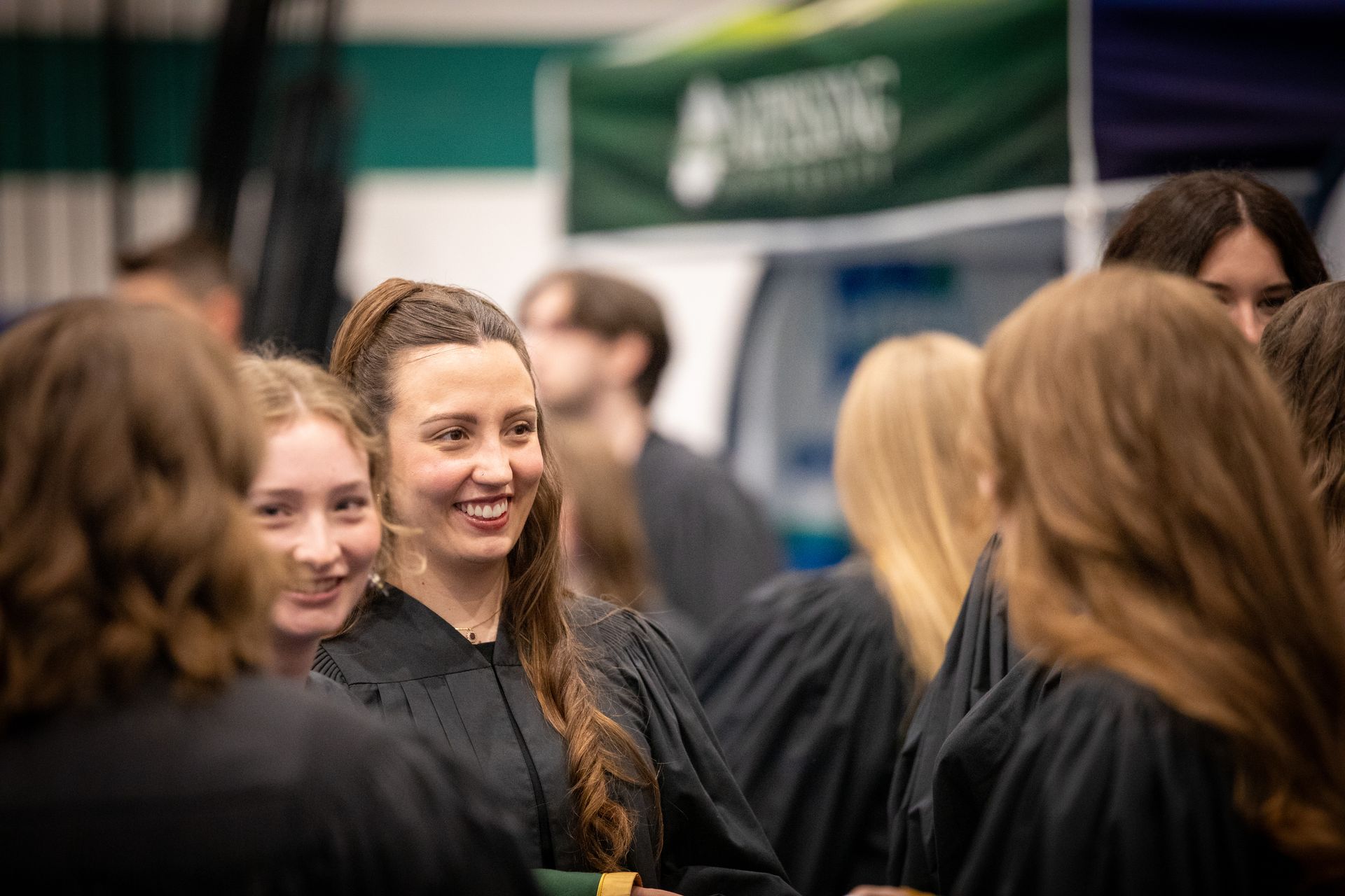 Woman smiling in a crowd at an indoor event, with a green banner in the background.
