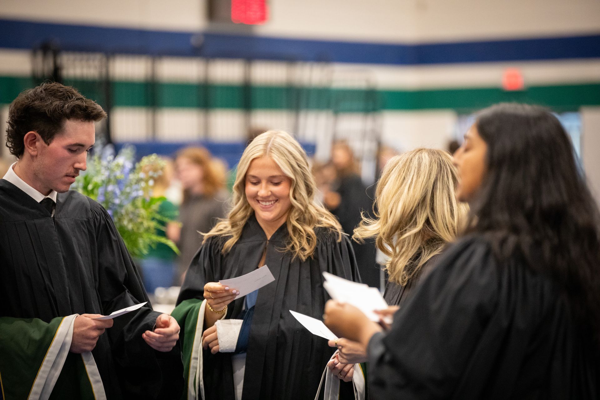 Graduates in gowns reading papers during a ceremony indoors
