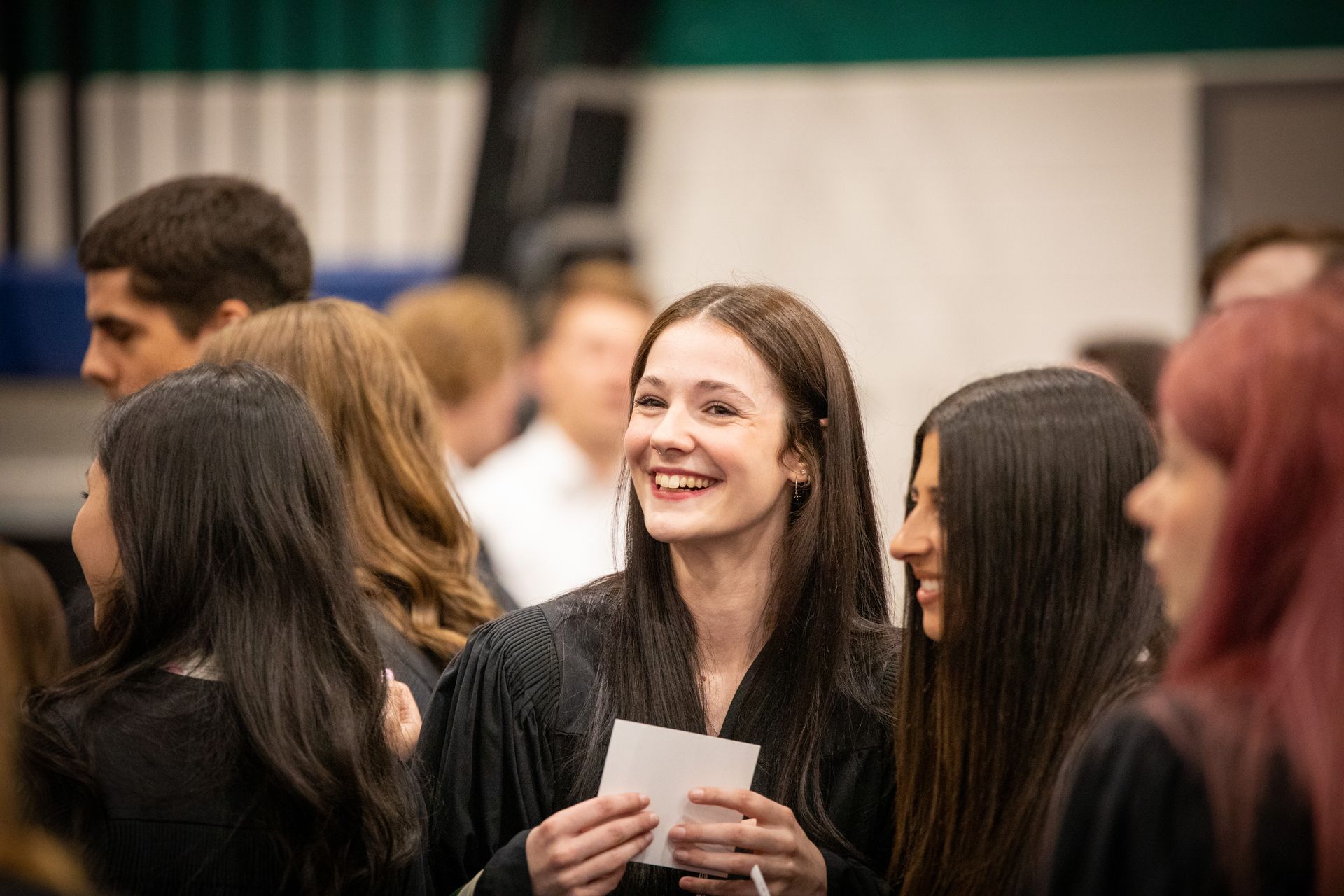Smiling woman holding a card among a crowd at an indoor event