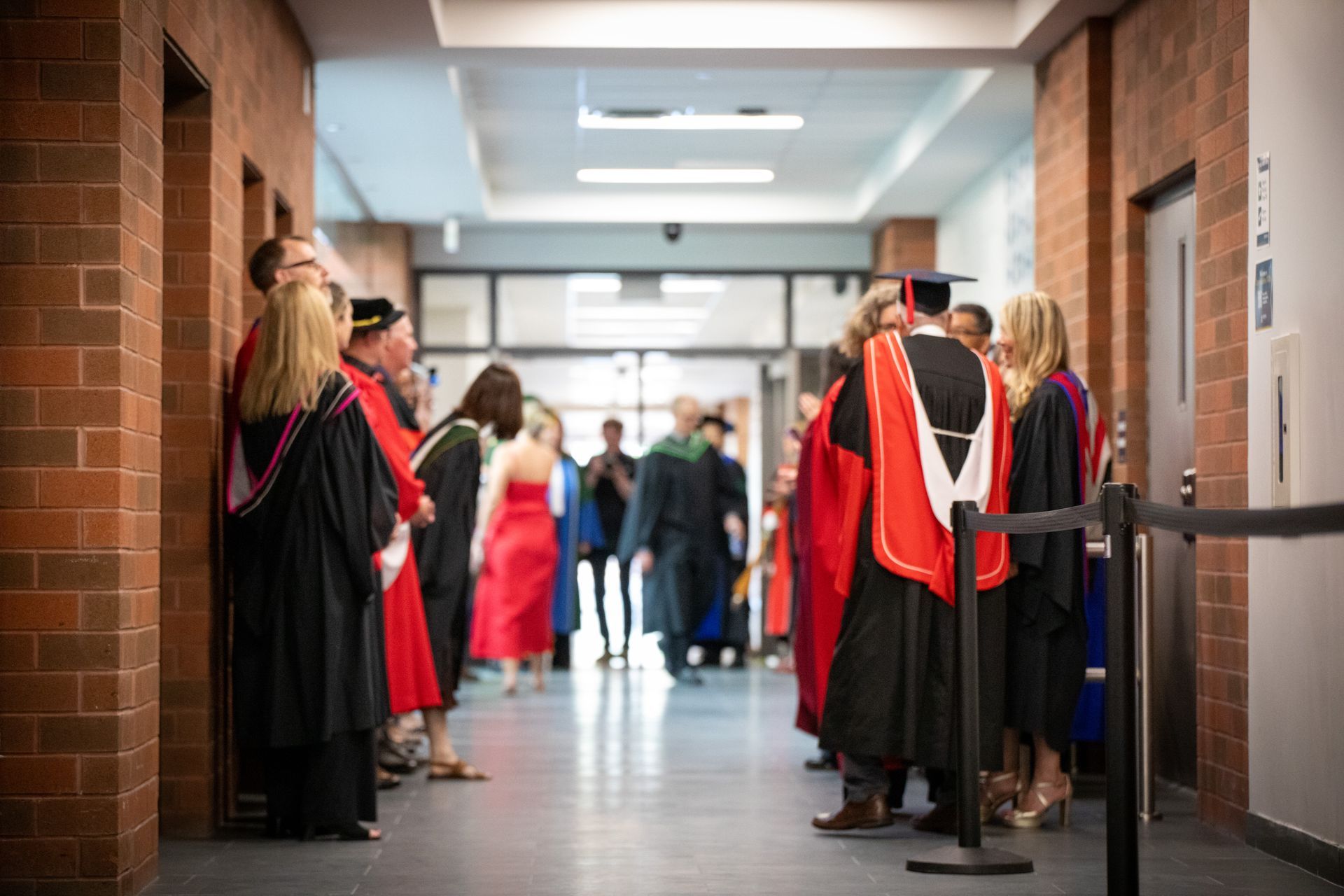 Graduates in red and black robes line a school hallway during a ceremony
