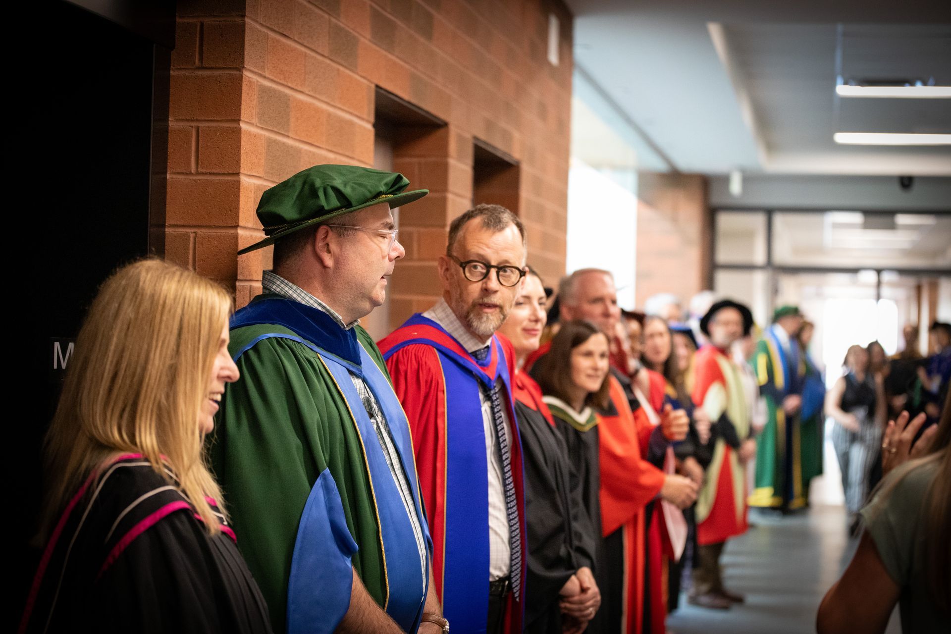 People in colorful academic robes standing in a hallway during a ceremony