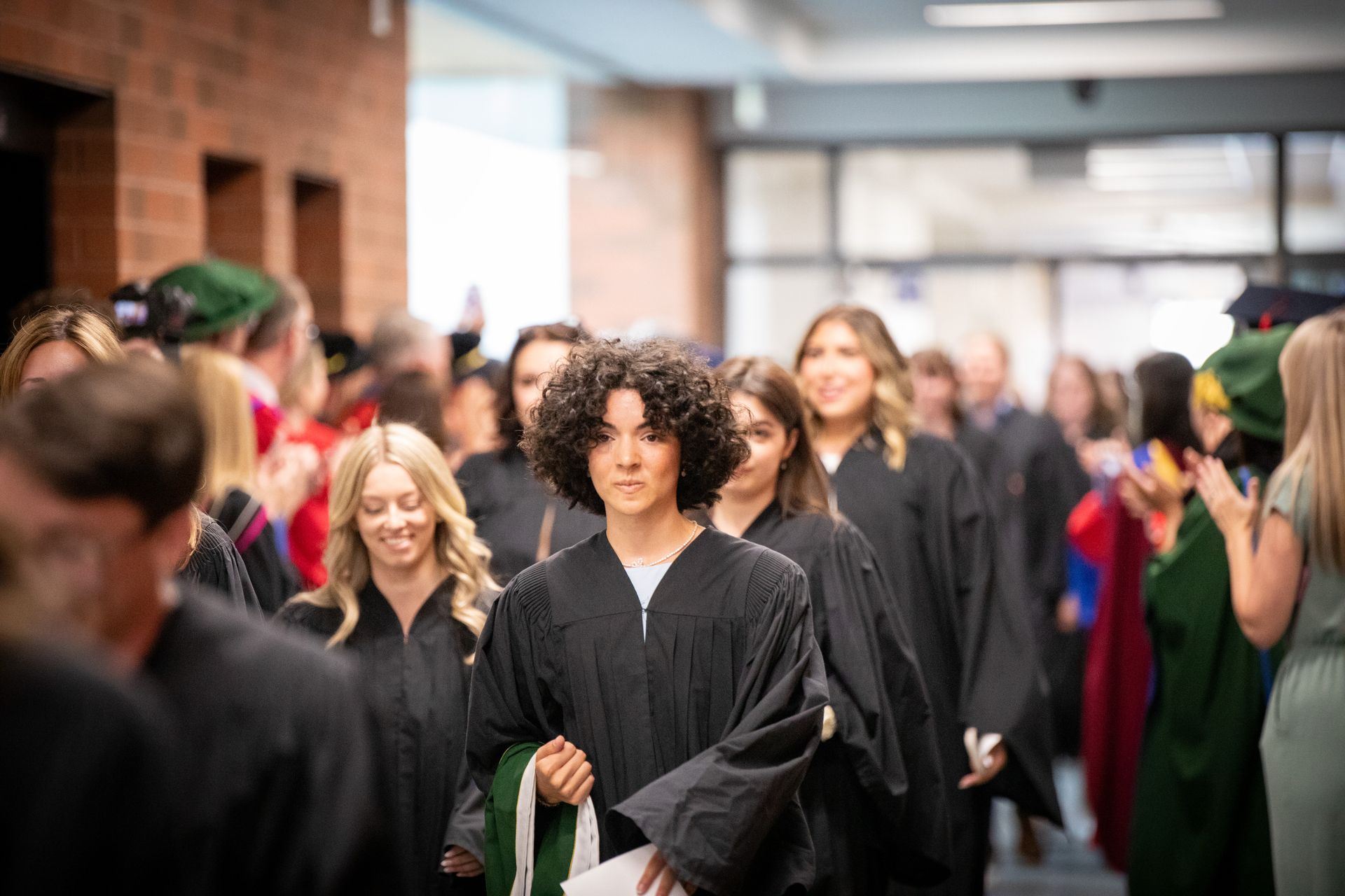 Graduates in black gowns walking through a hallway at a ceremony