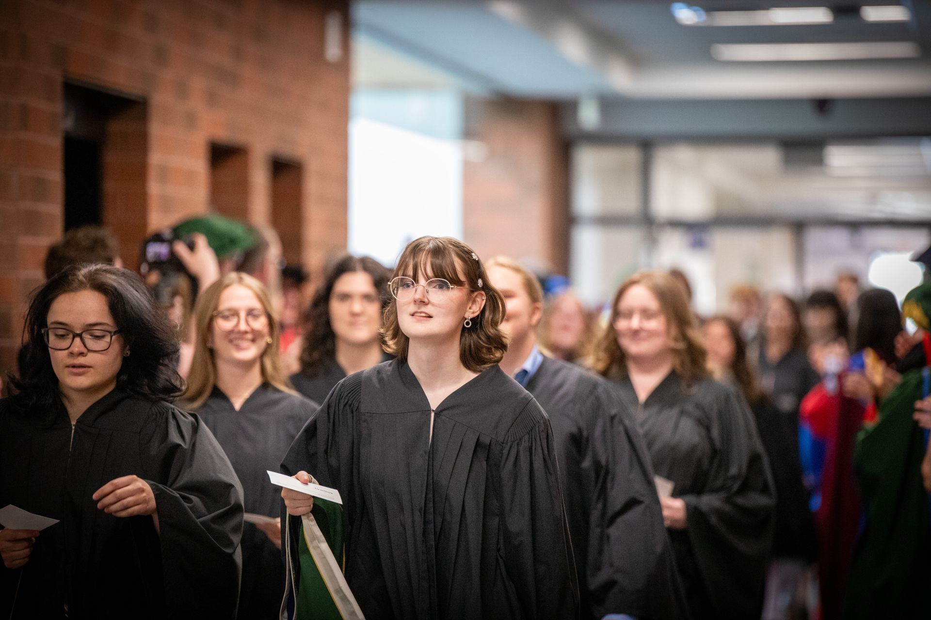Graduates in black gowns walking in a hallway during a ceremony procession