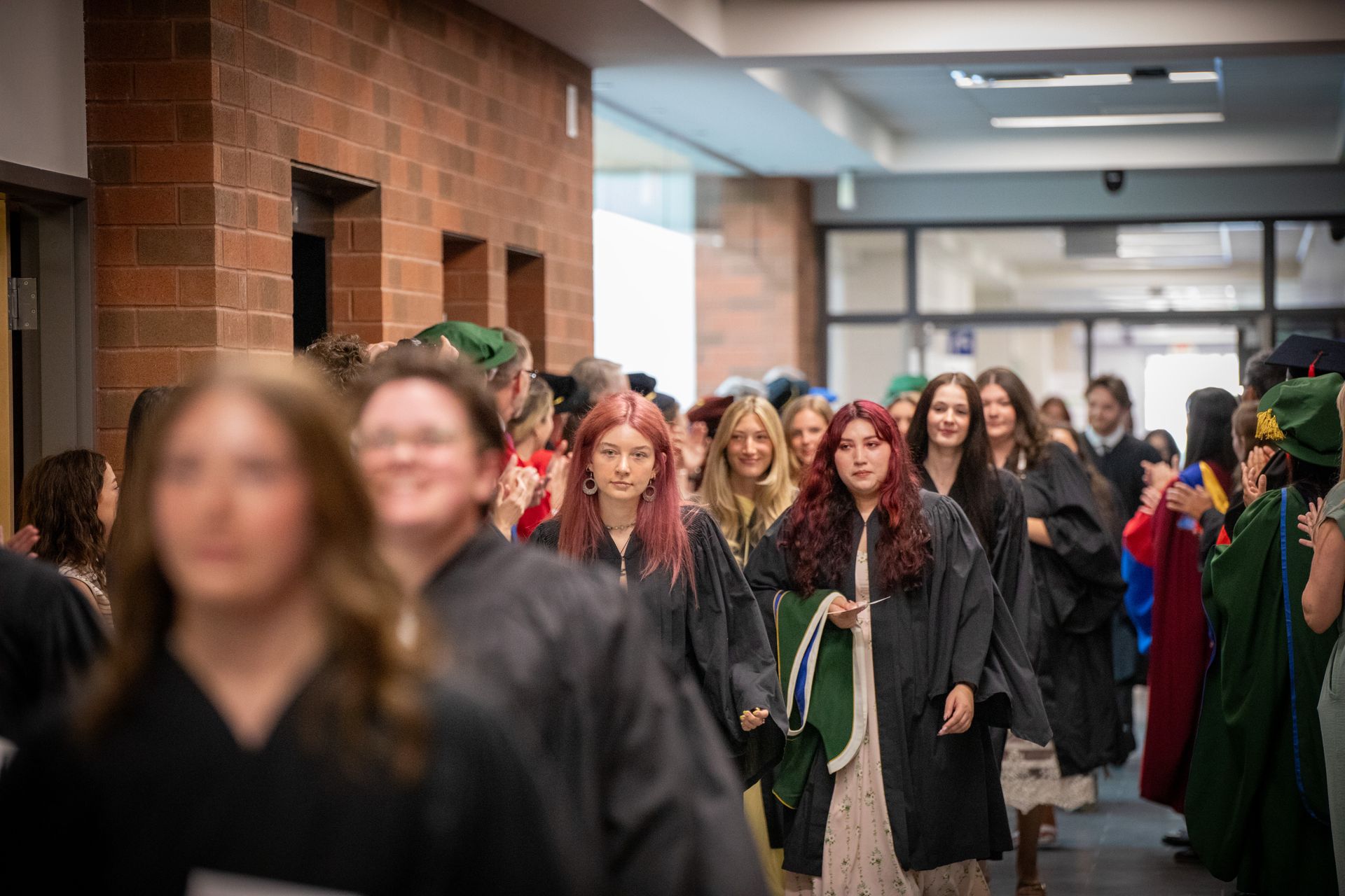 People in graduation gowns walking through a school hallway during a ceremony