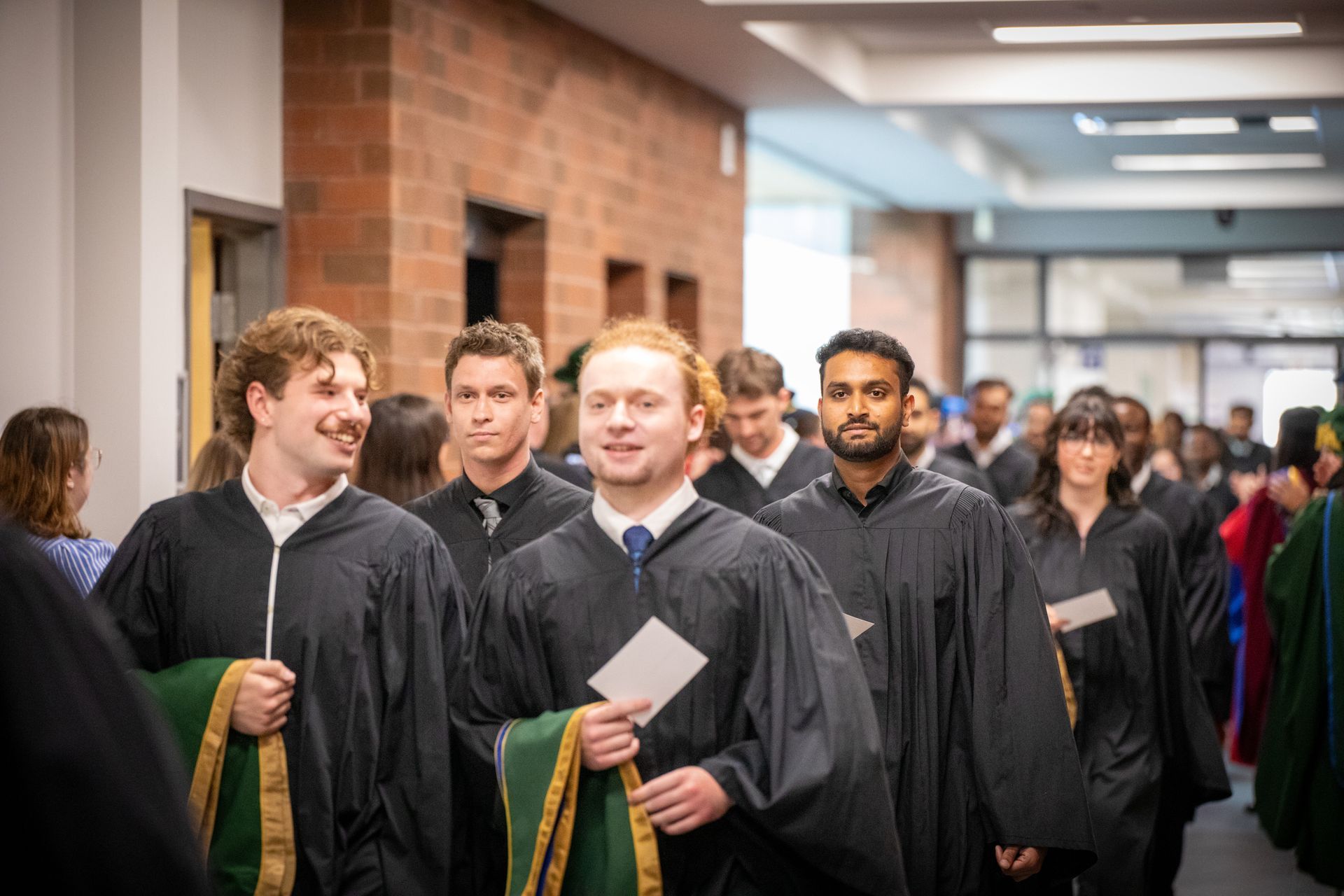 Graduates in black gowns walking through a school hallway during a ceremony