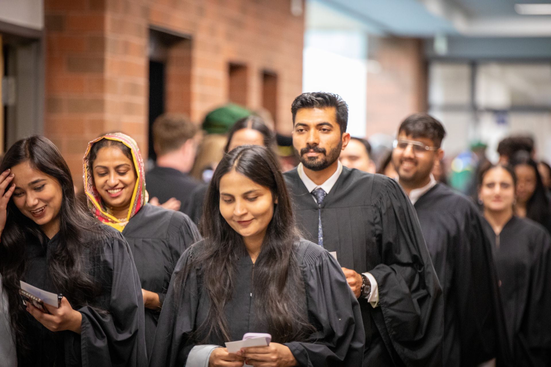 Graduates in black gowns and green stoles walking
