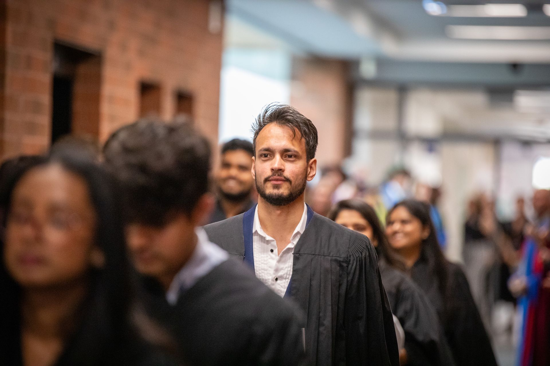 Crowd of people walking in a hallway, with a man in a dark robe centered in the foreground.