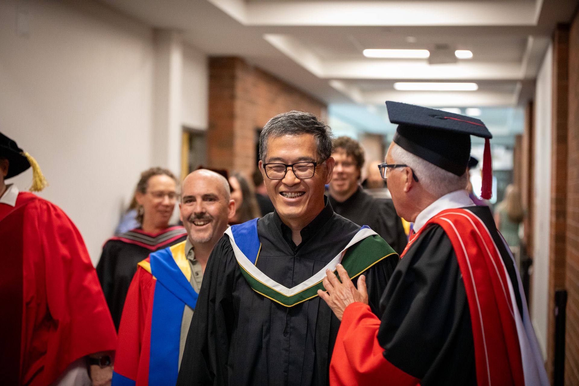 Graduate being congratulated in a hallway by faculty in academic regalia, smiling and shaking hands.