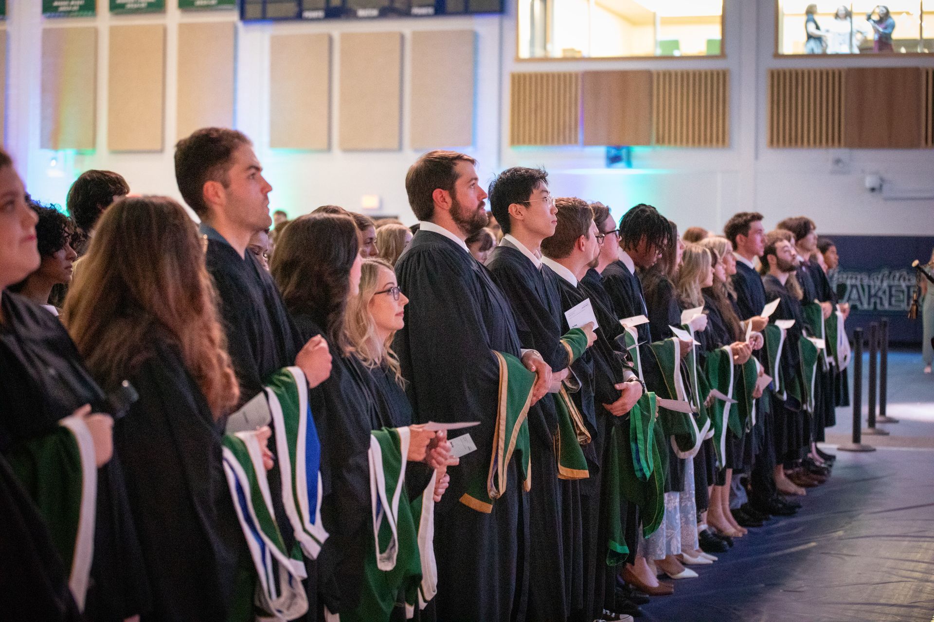 Graduates in black and green gowns facing forward during a ceremony