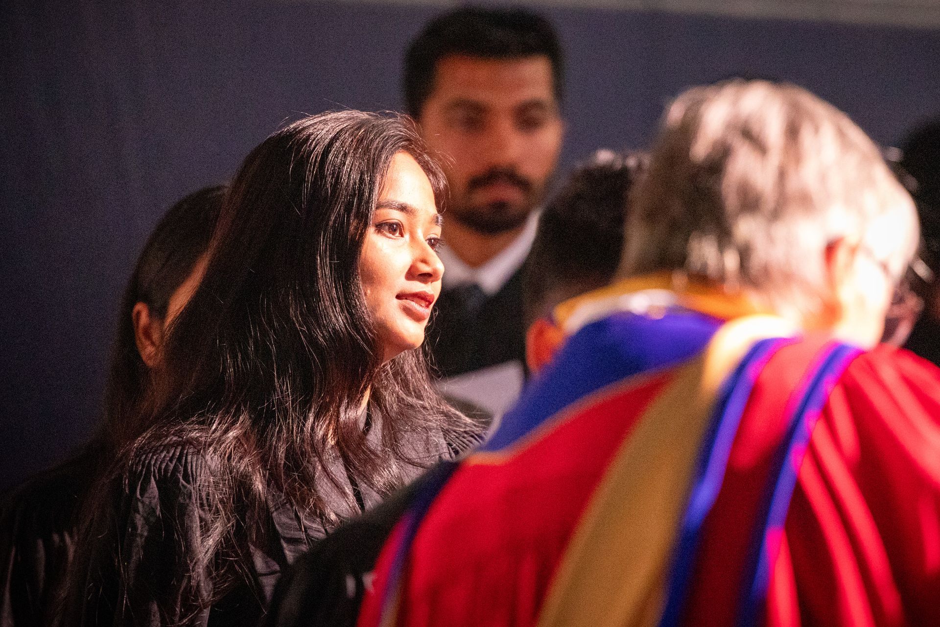 Woman in black smiles in a crowd, with blurred people in colorful clothing around her.