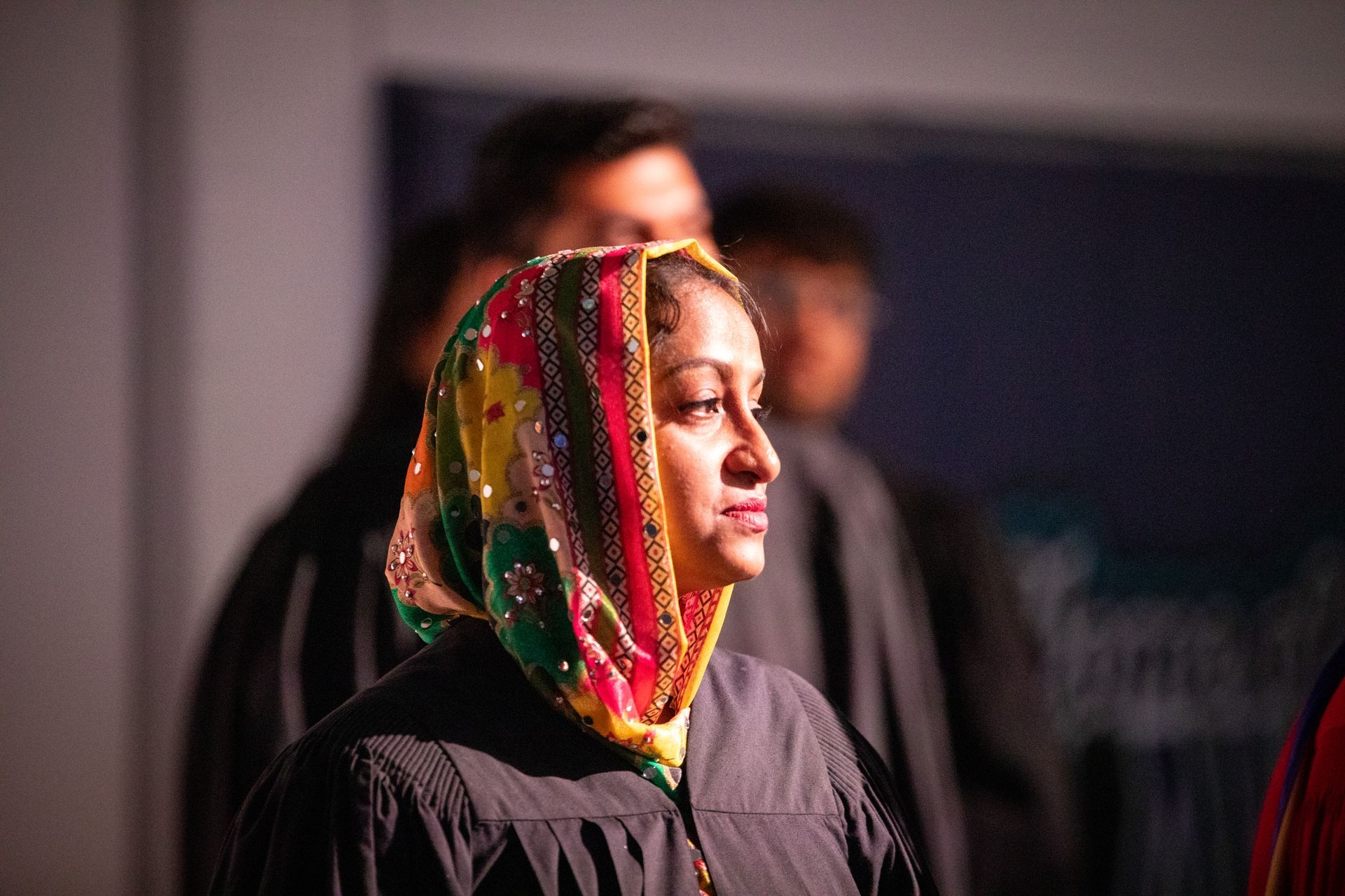 Woman in a colorful headscarf on stage, standing in profile with a focused expression.