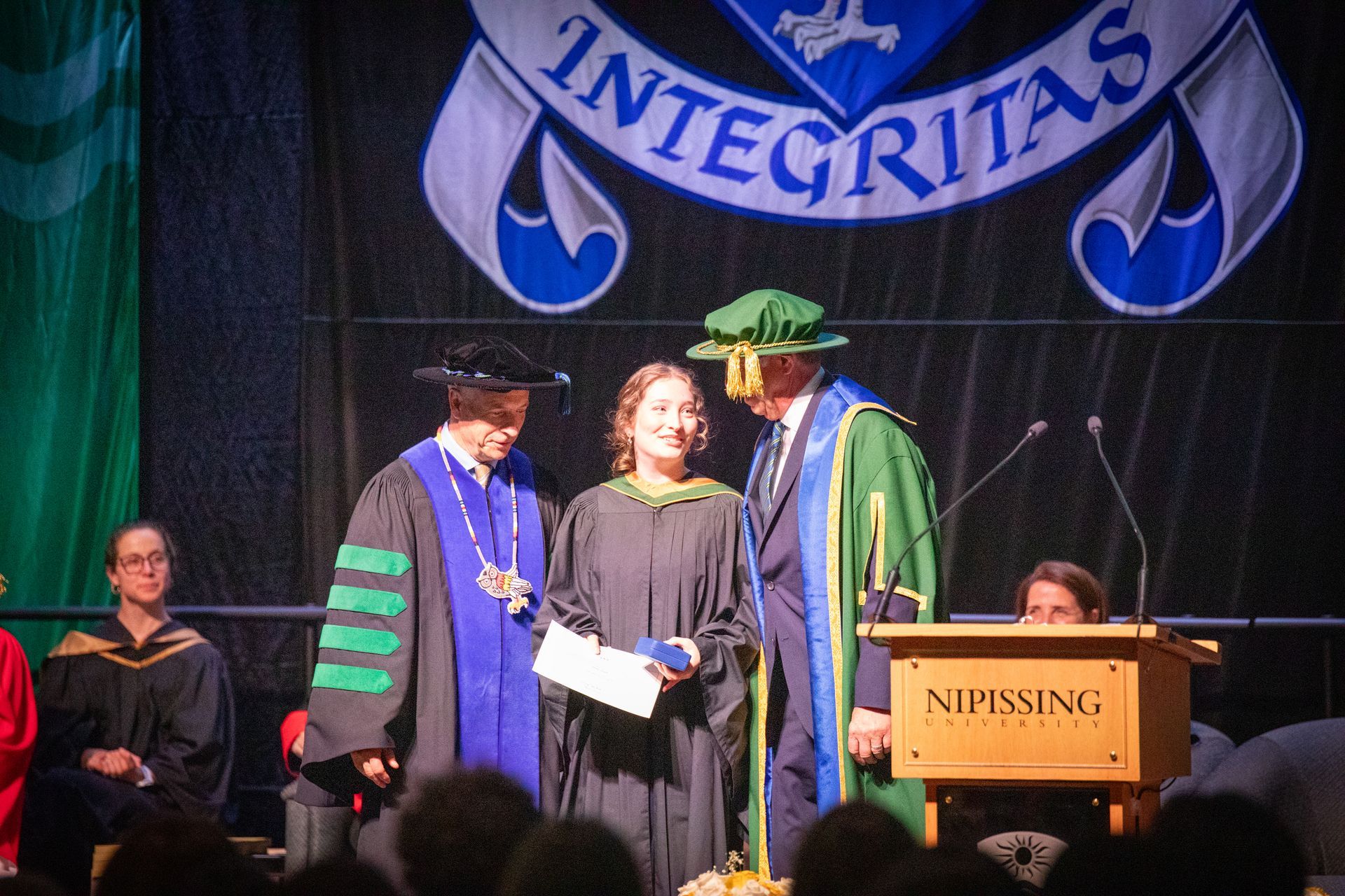 Graduation ceremony on stage with two faculty in robes presenting an award to a graduate at a podium