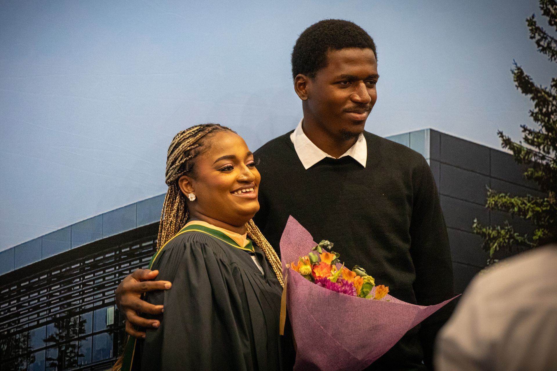 Two people posing, smiling and holding a bouquet of flowers.