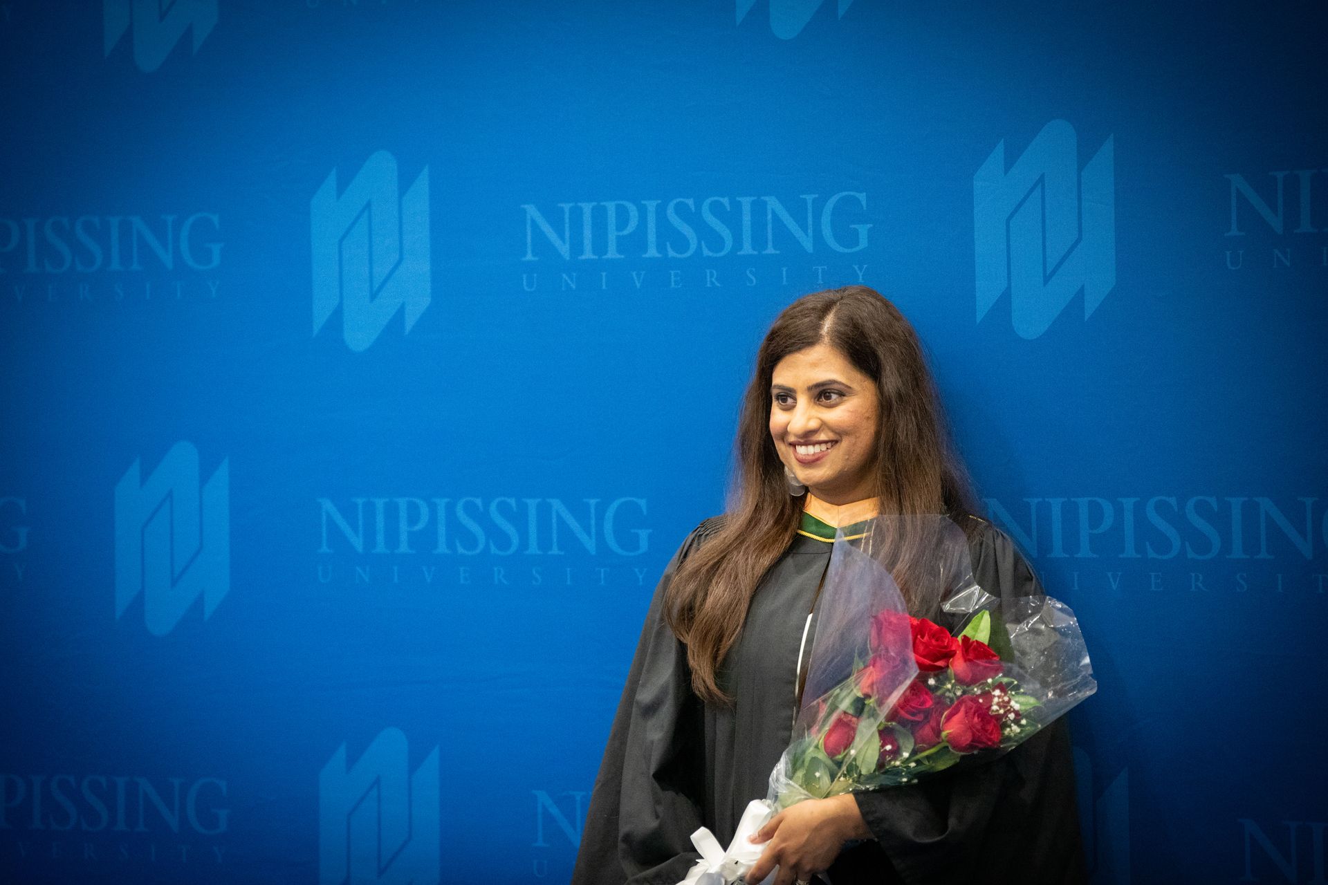 Woman holding a bouquet in front of a blue Nipissing University backdrop
