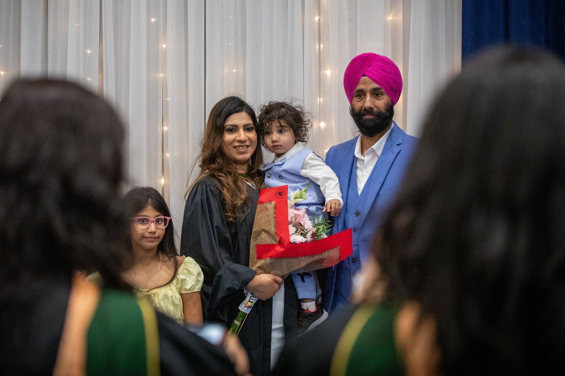 Family posing at an indoor celebration, holding a baby and a gift, with guests in the foreground
