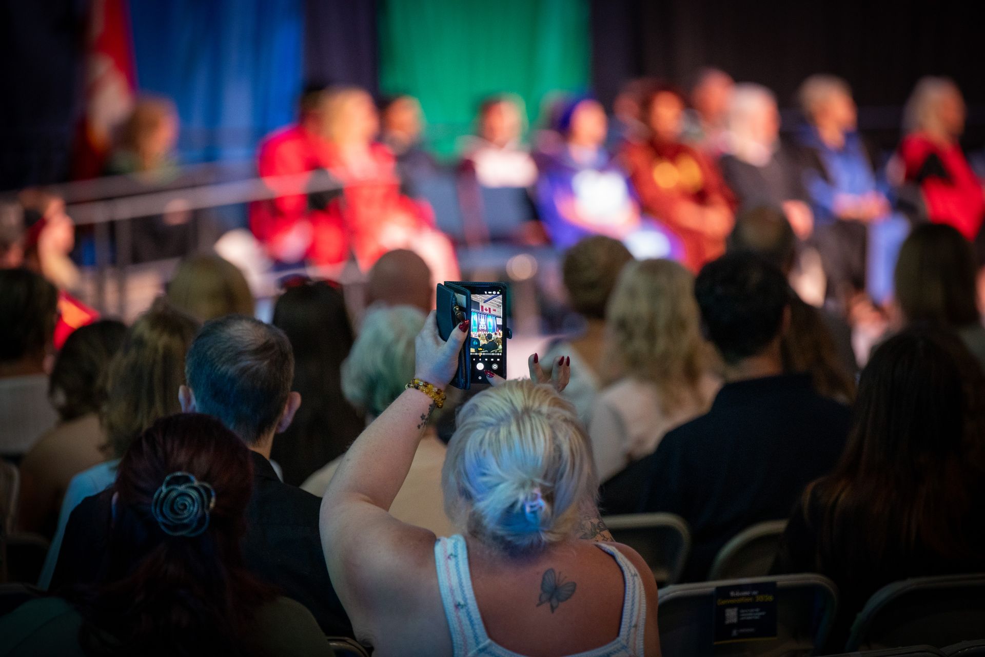 Audience member recording a blurred stage panel with a smartphone 
