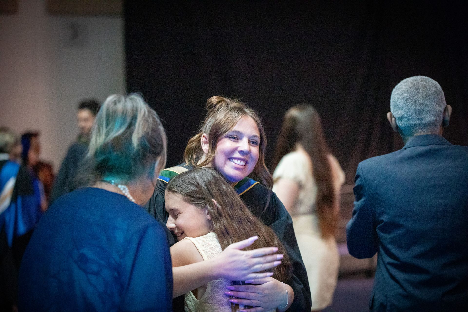 People hugging and smiling at a social gathering in a dimly lit room