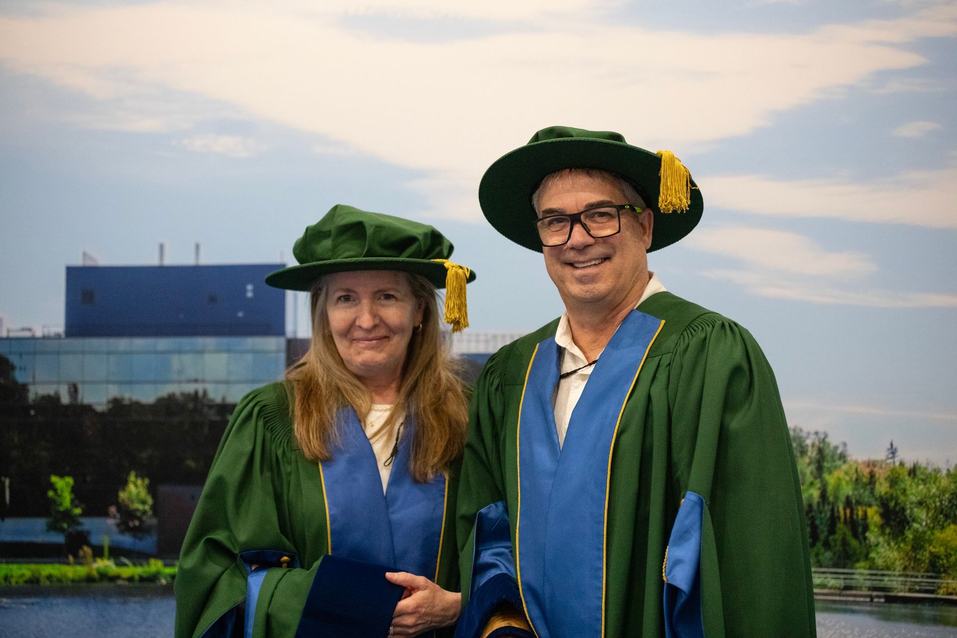 Two graduates in green gowns and hats smiling
