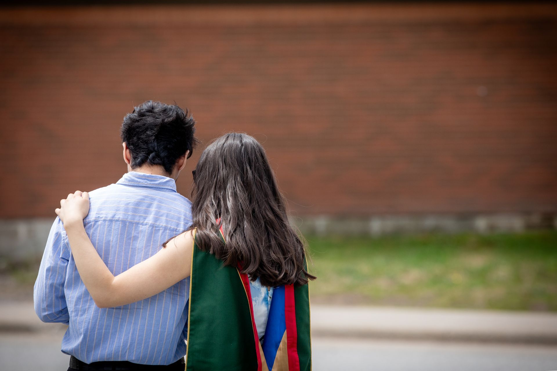 Two people walking, seen from behind, in front of a brick wall.