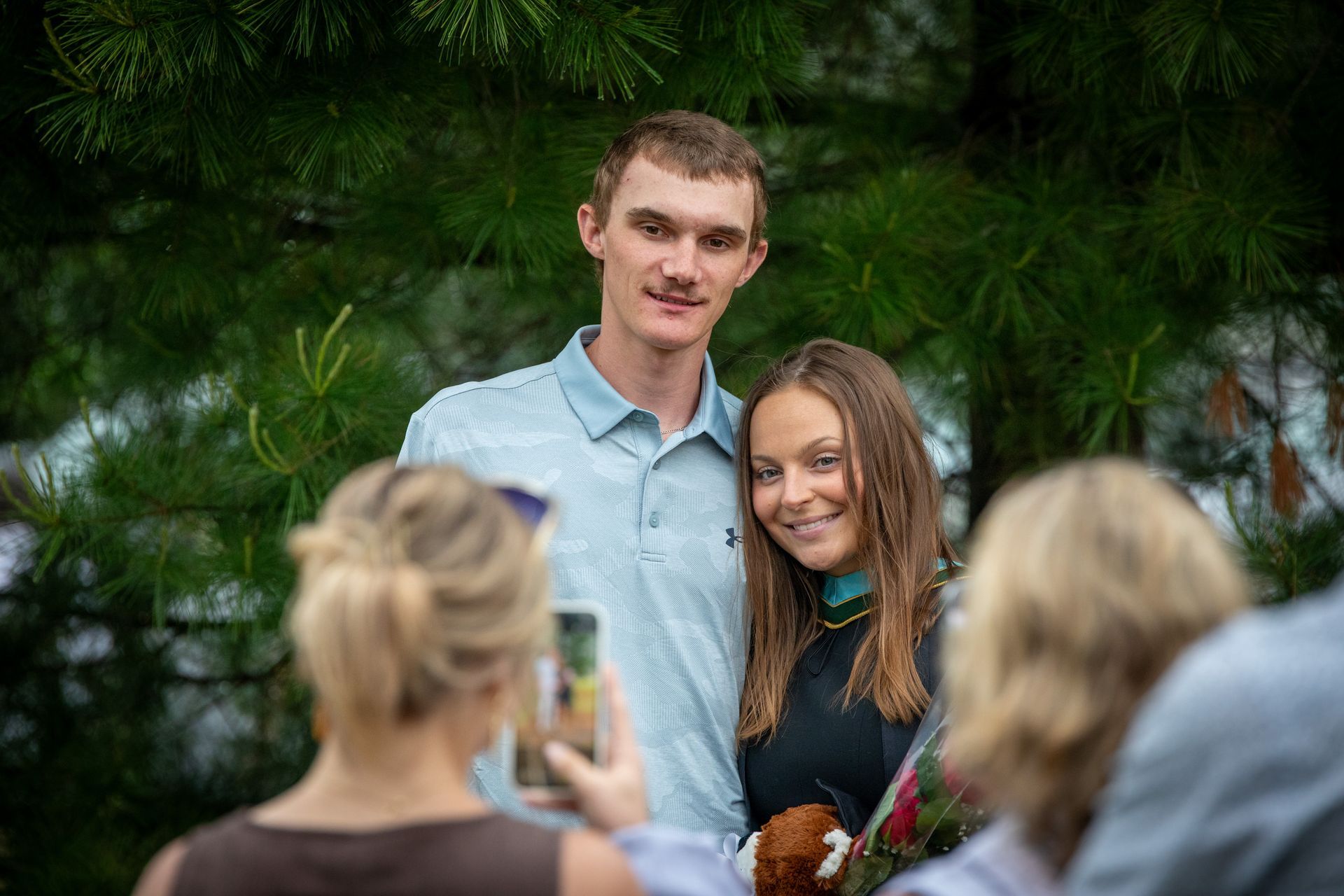 Couple posing for a photo outdoors, with one person holding flowers and others in the foreground taking pictures