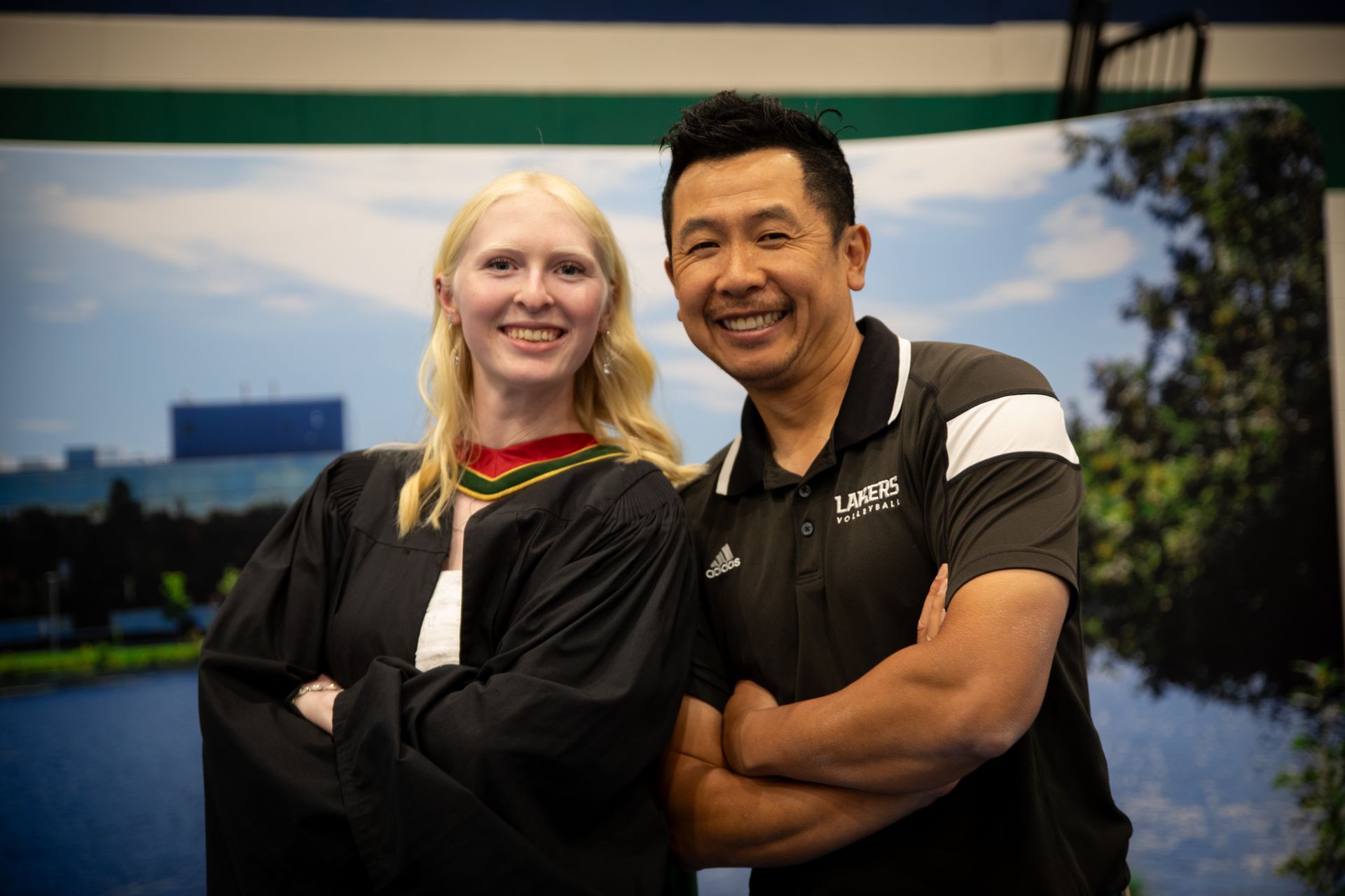 Two smiling people standing with arms crossed at an indoor event backdrop