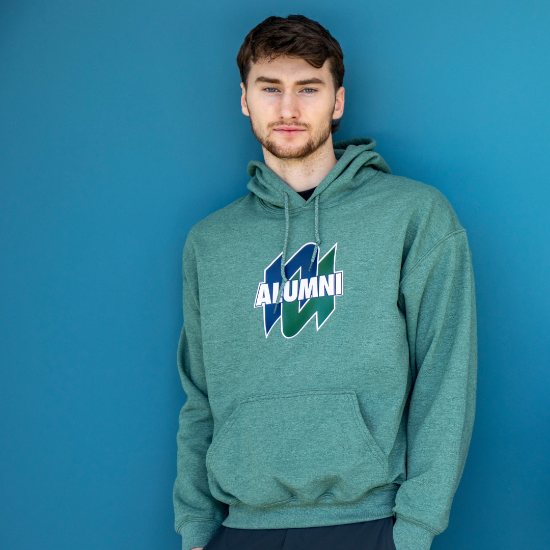 Man in a green ALUMNI hoodie standing against a blue wall
