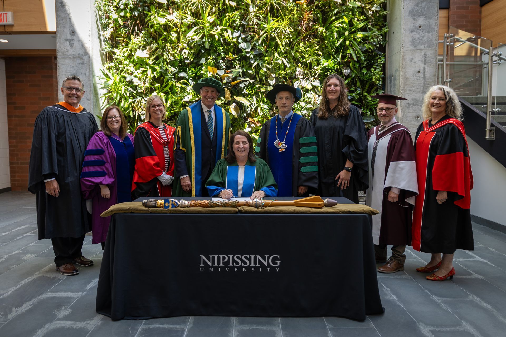 Group of people in academic regalia posing behind a Nipissing University table.