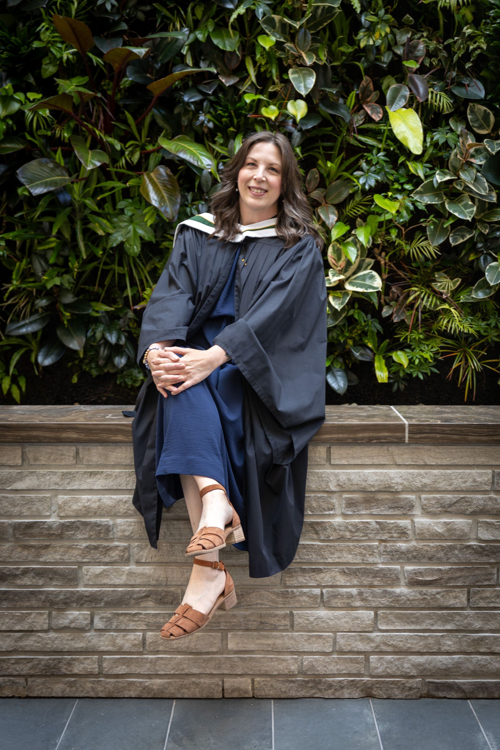 Woman sitting on a brick ledge in front of a green leafy wall
