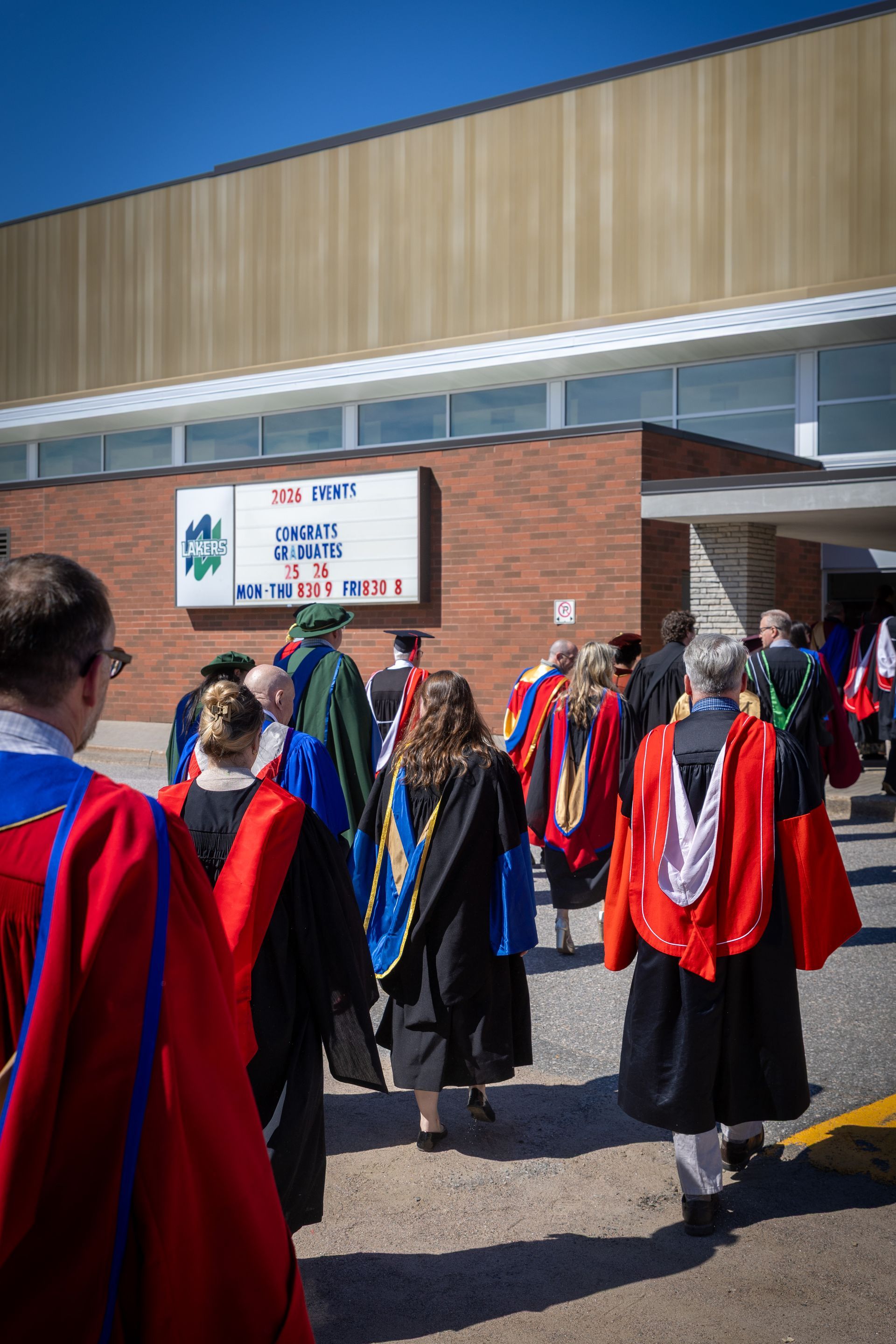 Faculty gather outside a building under a blue sky.