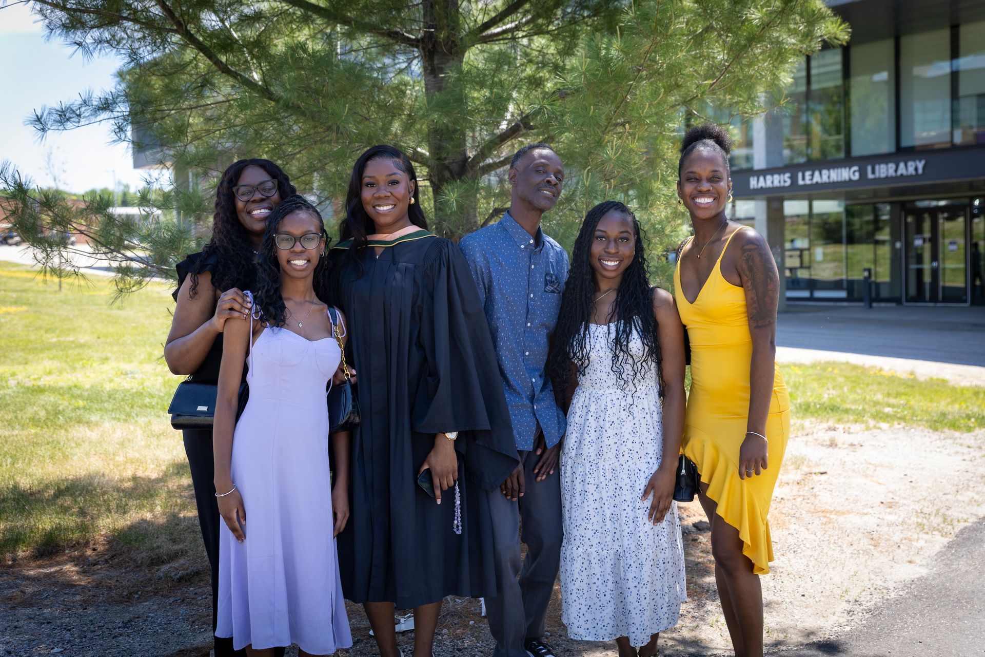 Six people posing outdoors in front of a library building, dressed in formal attire.