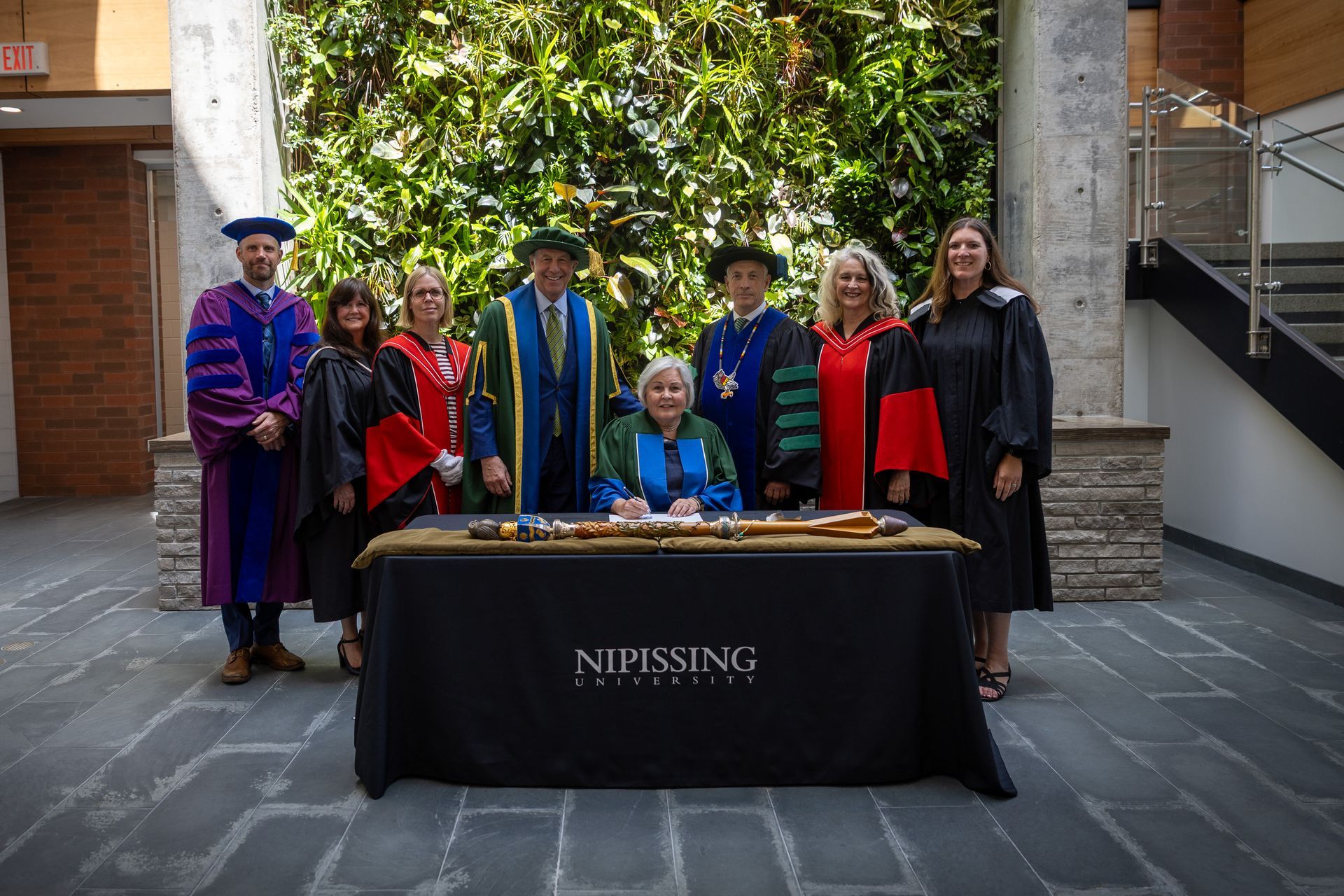 Group in academic robes standing behind a table labeled “Nipissing University” 