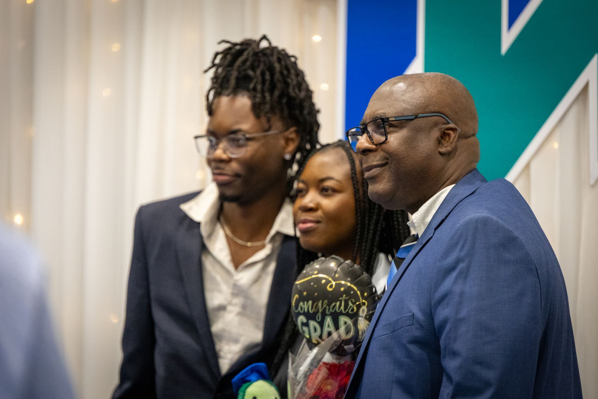 Three people posing together at an event, smiling in front of a blue-and-white backdrop.