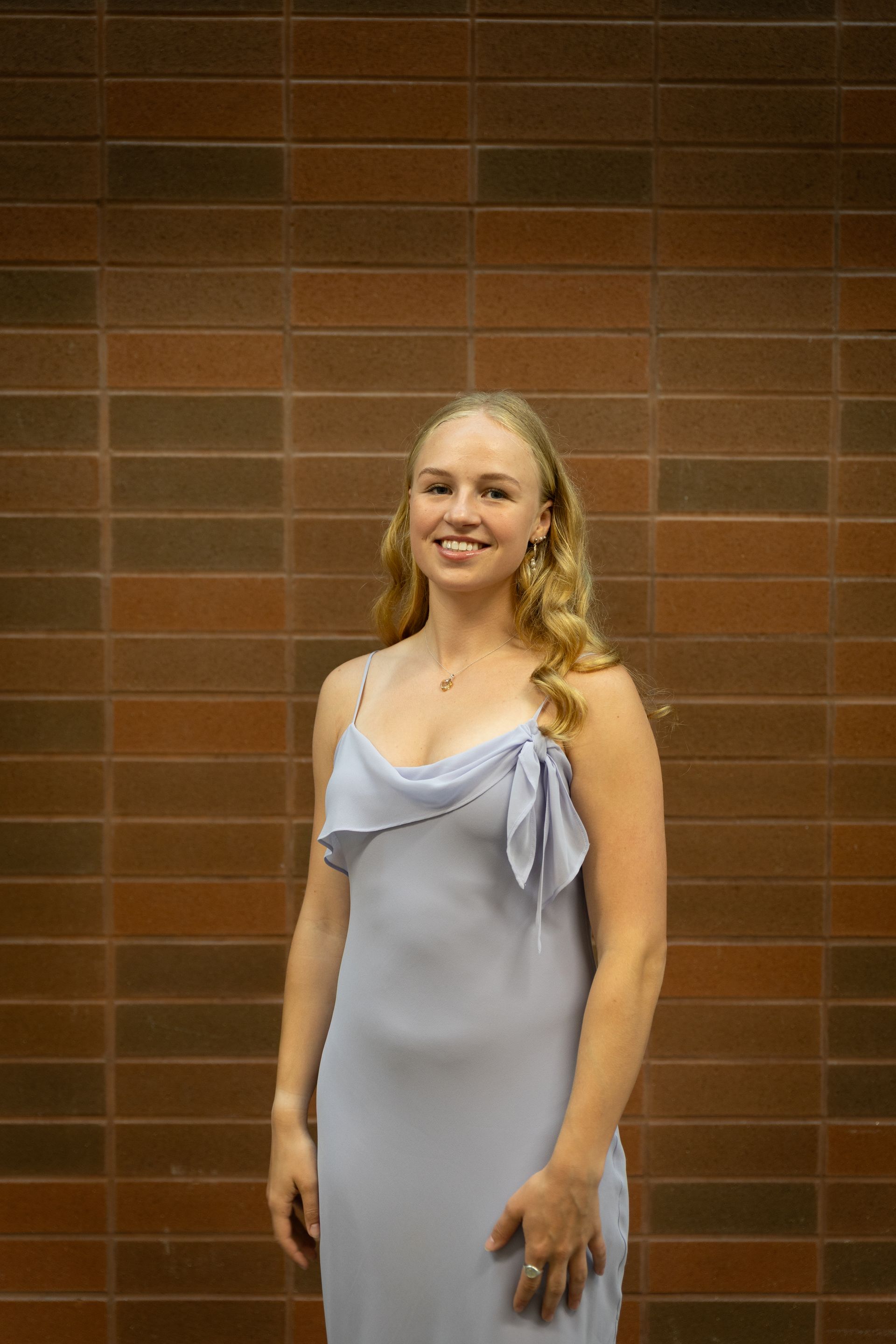 Woman in a light blue dress smiling in front of a brick wall.