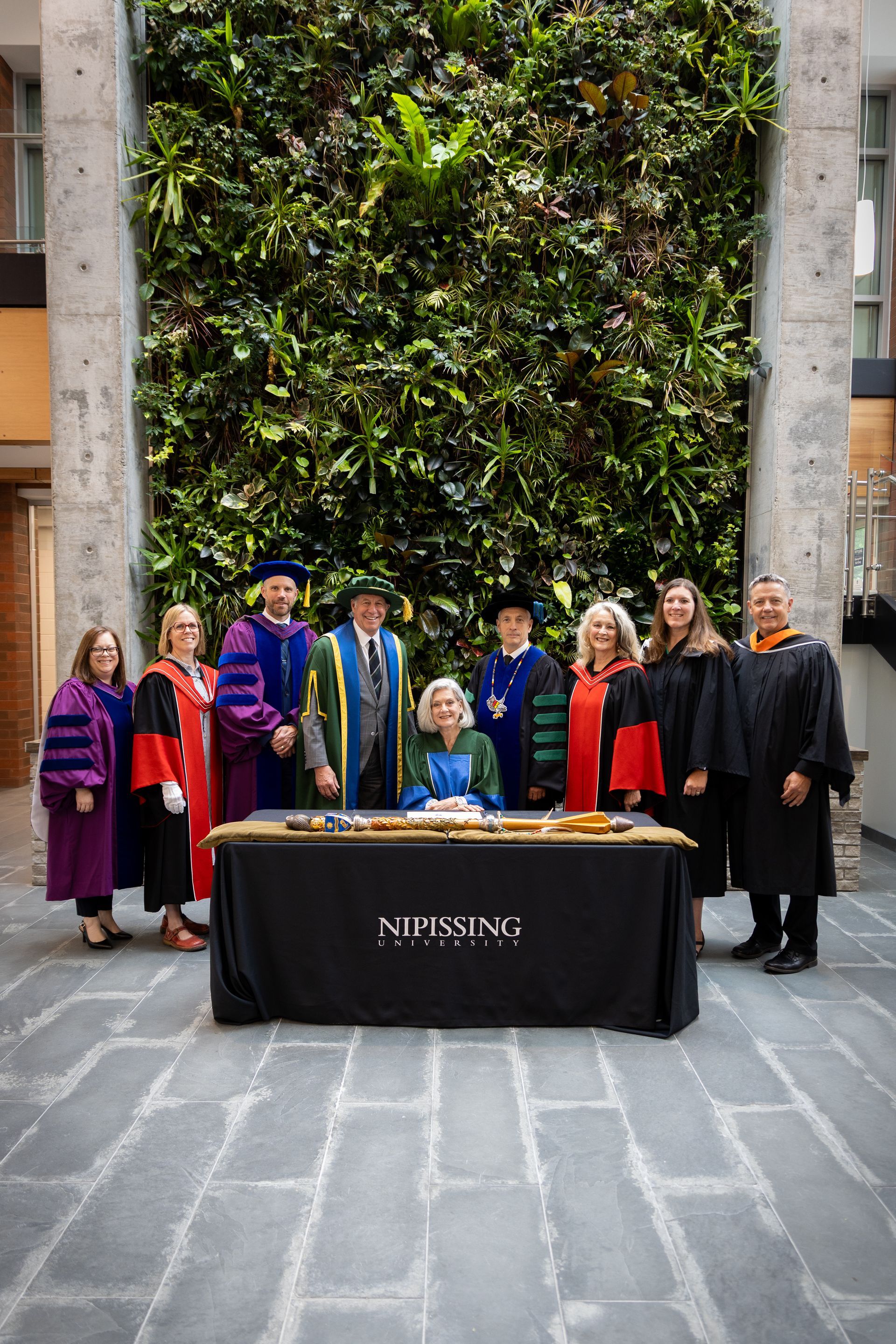 Group posing indoors beside a table in front of a tall green living wall