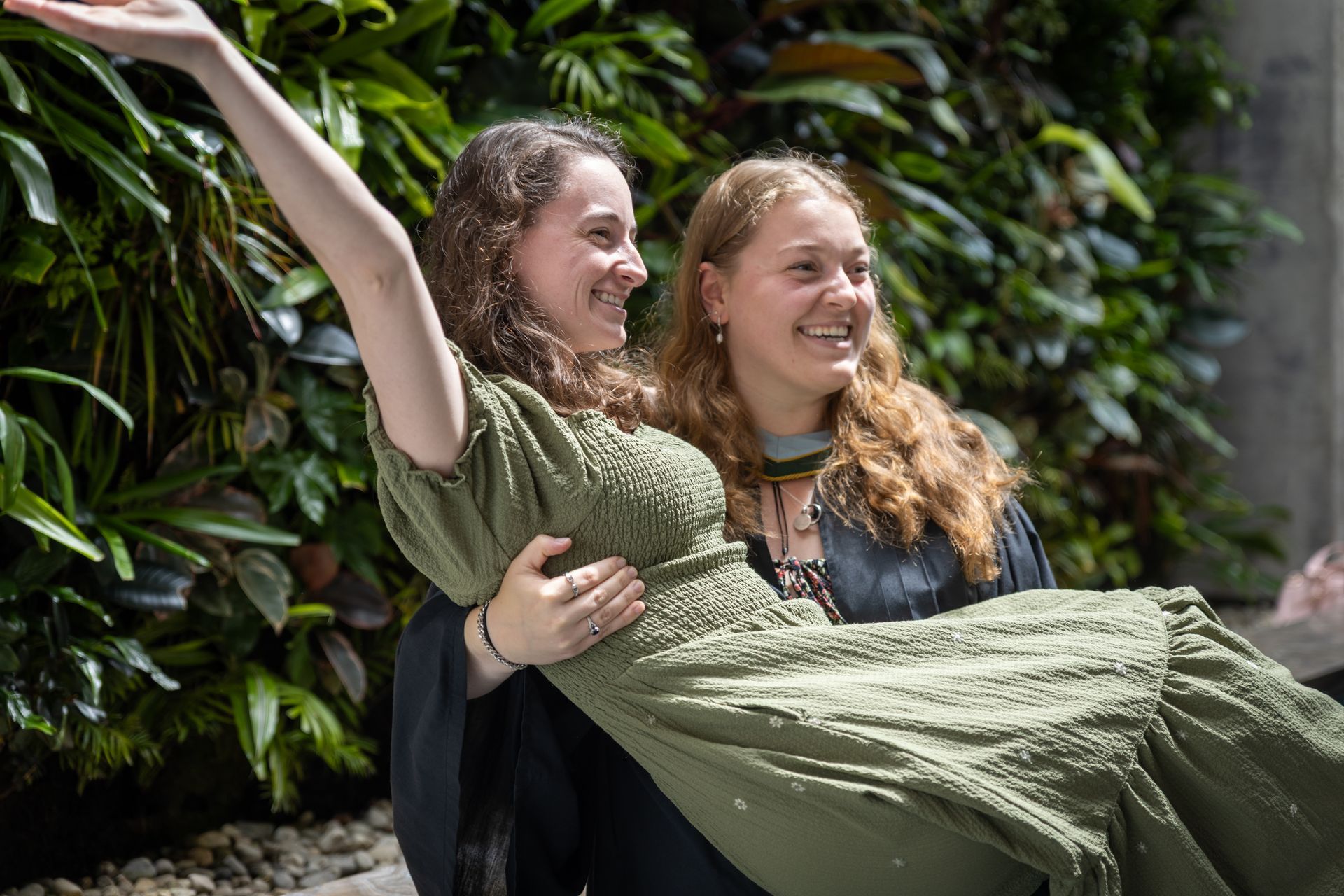 Two smiling people, one lifting the other in a green dress with arms raised.