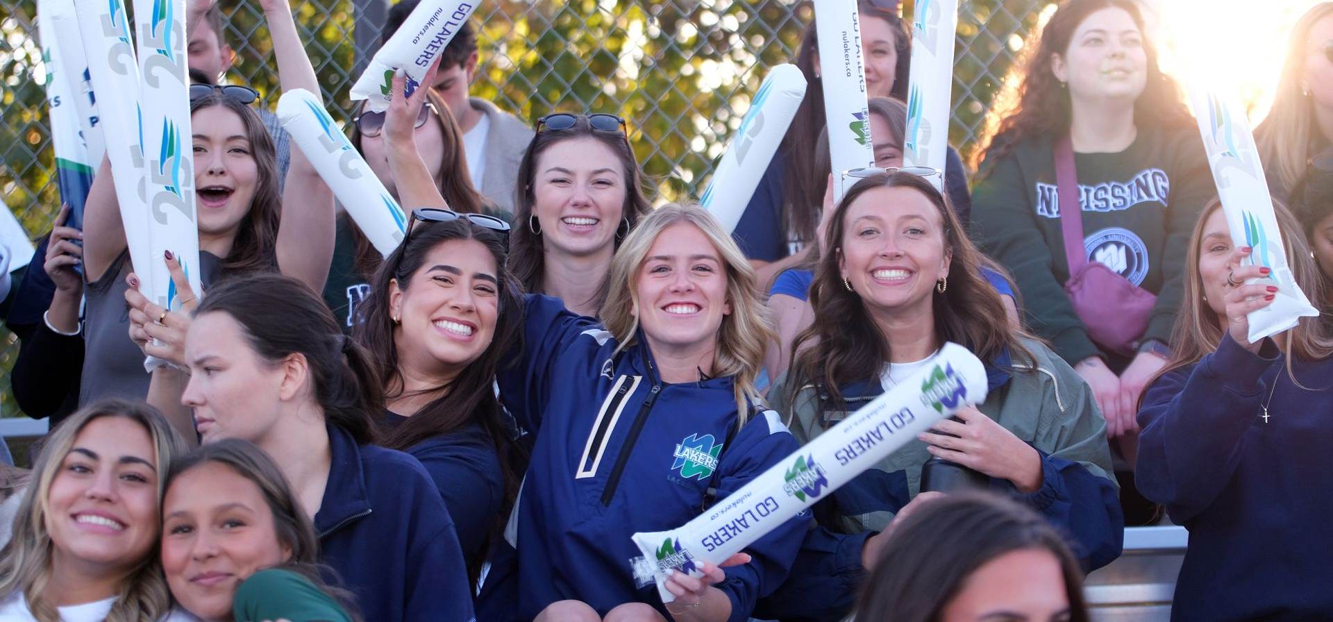 Group of smiling people posing outdoors, holding white signs and cheering in blue clothing