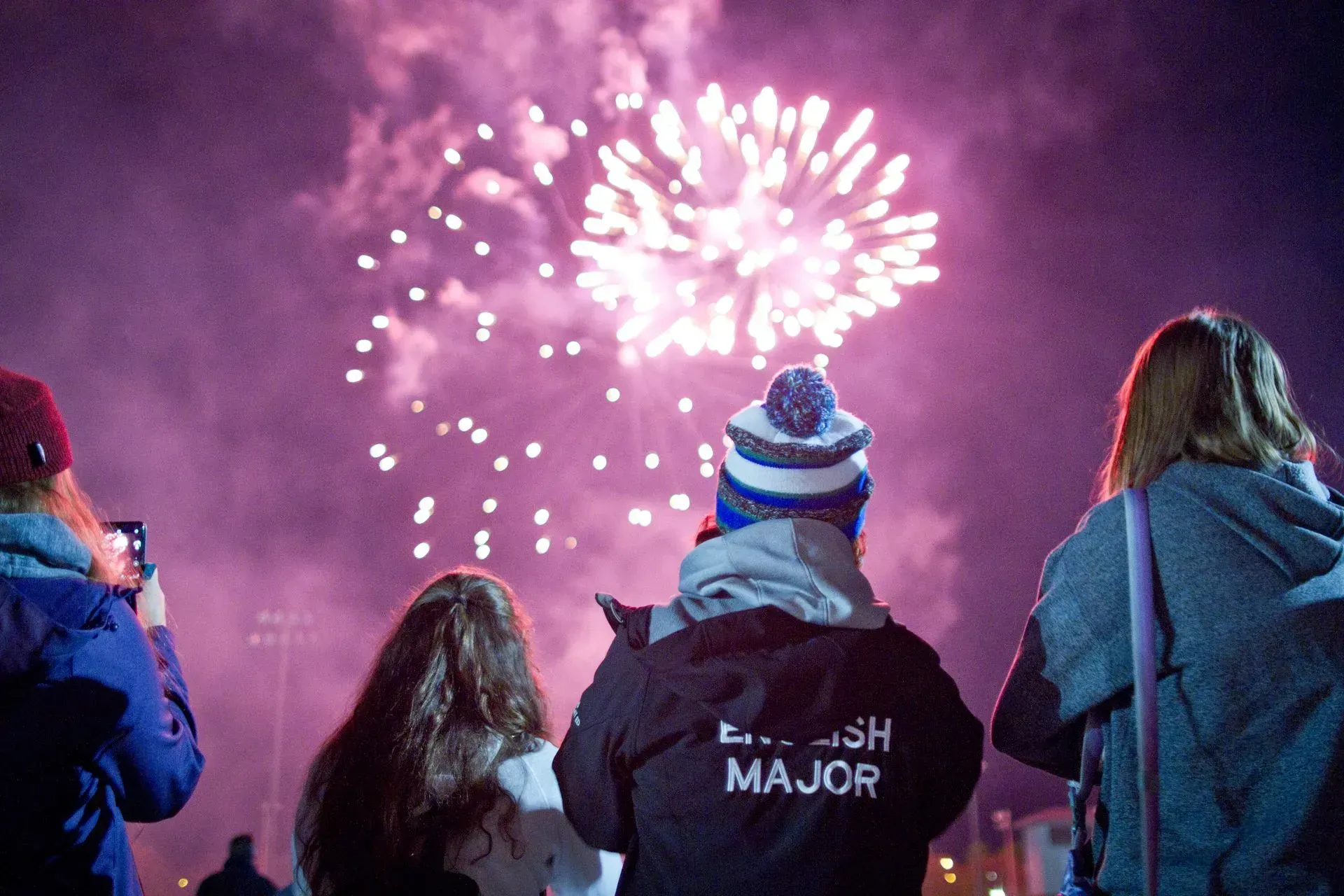 Three people watching pink fireworks over a snowy night scene