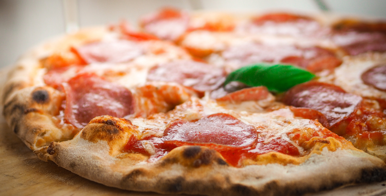 Close-up of a pepperoni pizza with melted cheese and basil on a wooden board