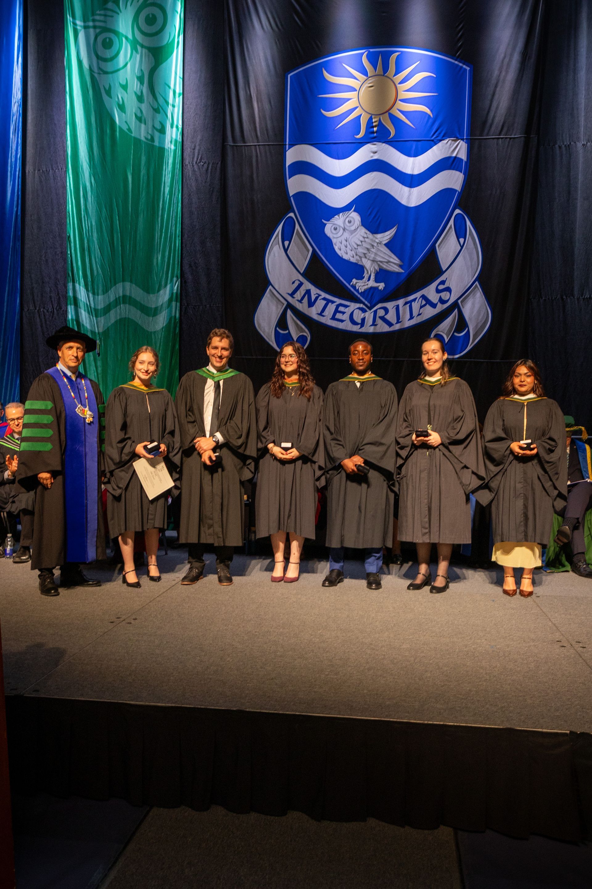 Graduates in gowns onstage with a university crest backdrop