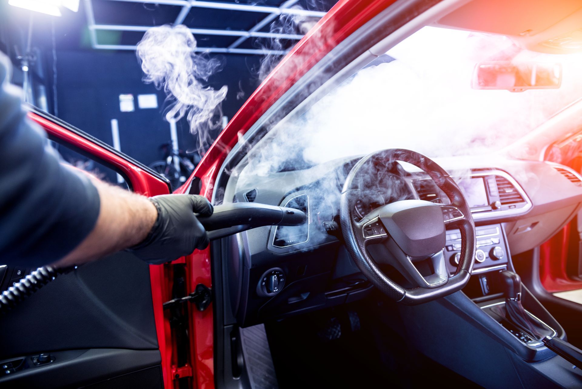 A person steaming a red car interior, removing dirt with a cleaning tool.