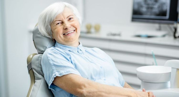 An elderly woman is sitting in a dental chair and smiling.