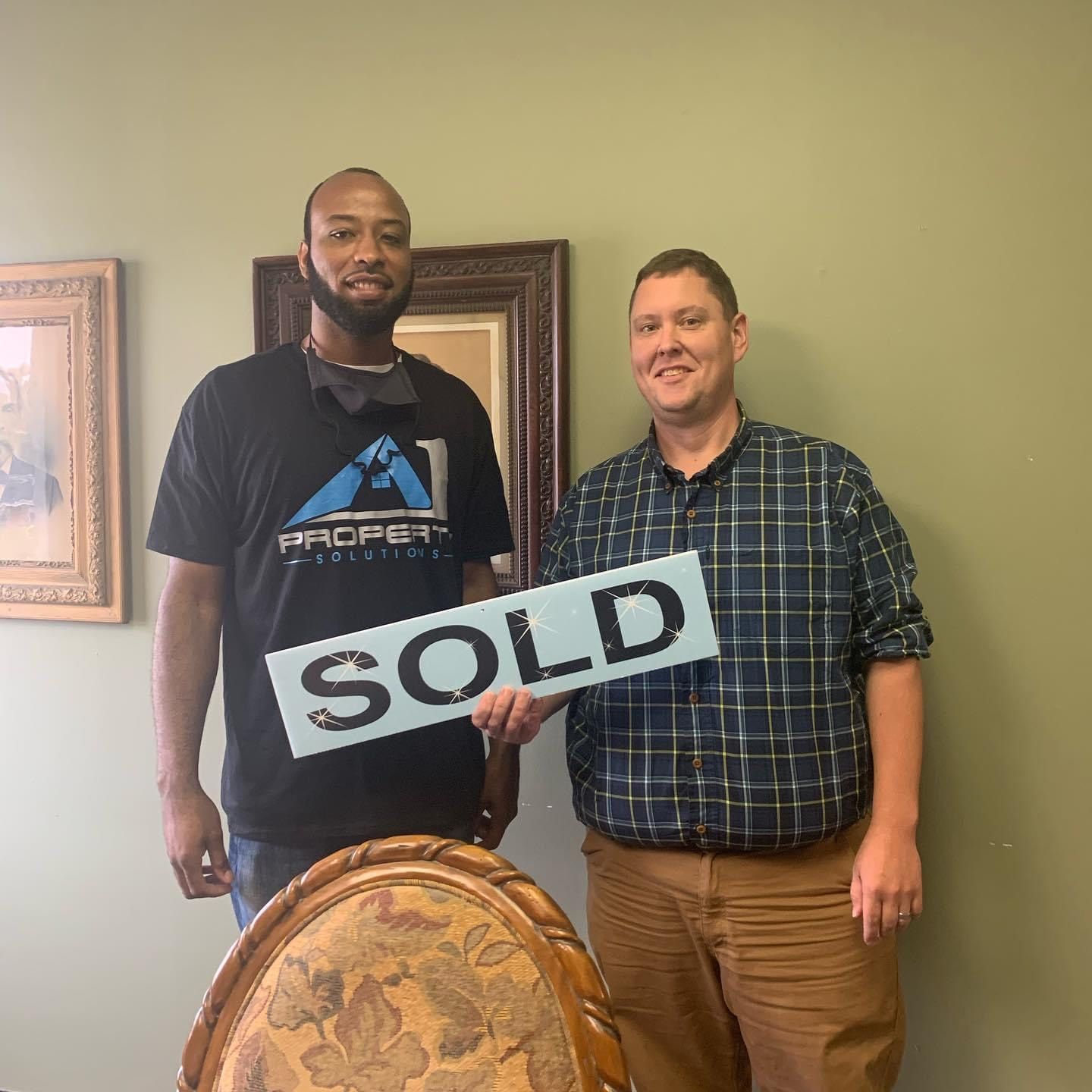 Two men are standing next to each other holding a sold sign.