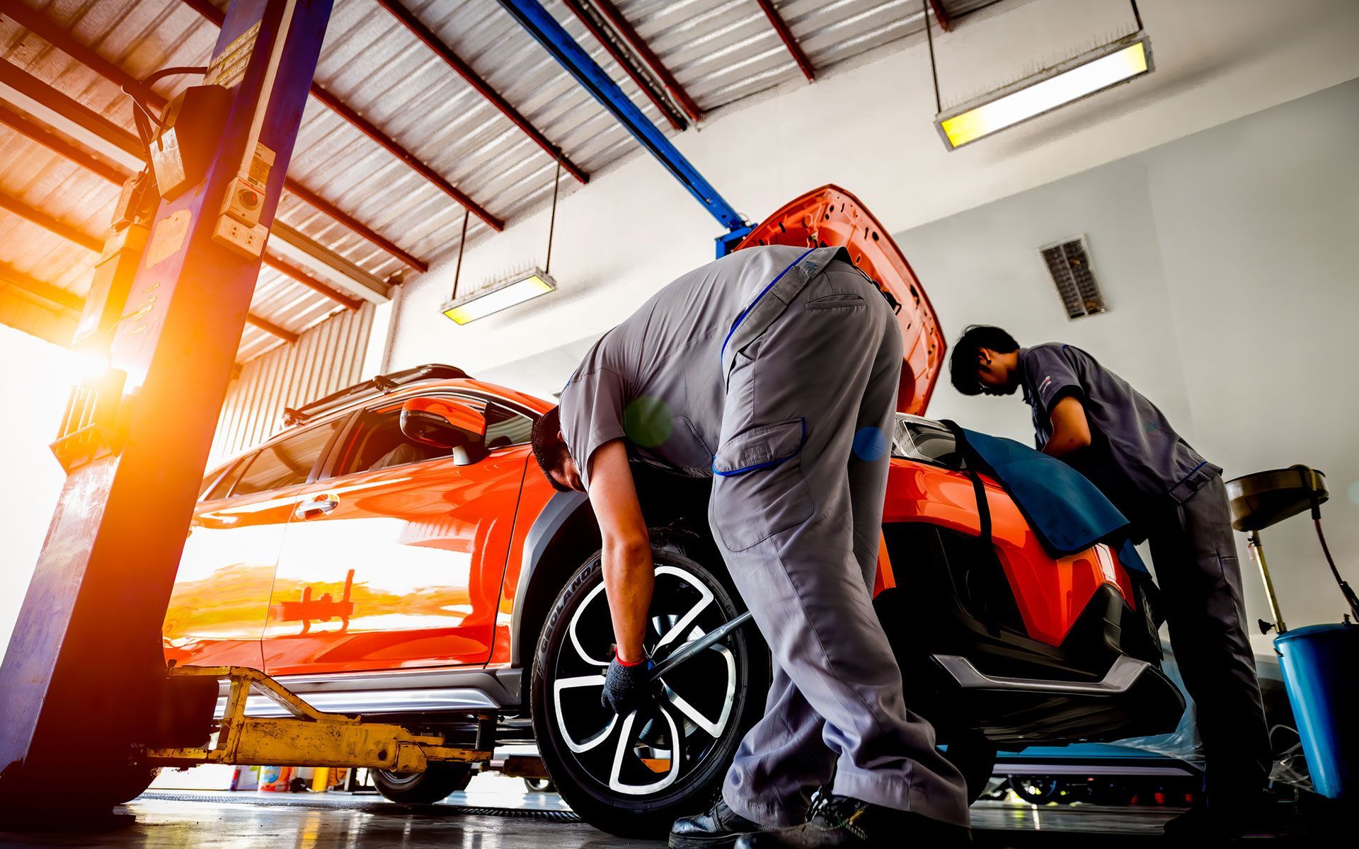 Two mechanics are working on a red car in a garage.