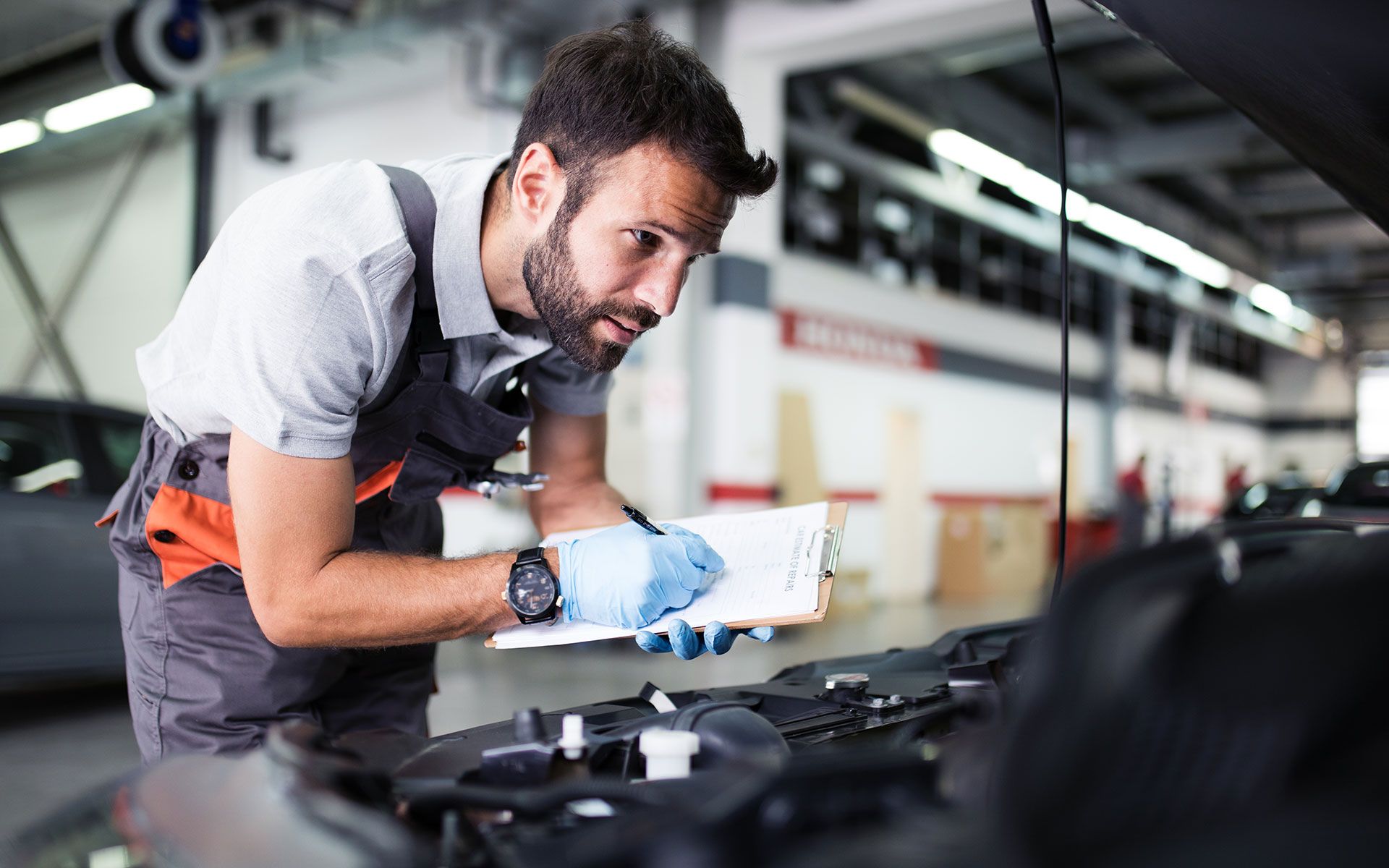 A man is looking under the hood of a car in a garage.