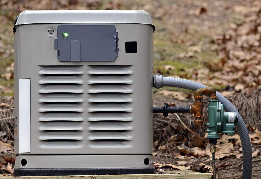 Gray residential backup generator with gas line outdoors.